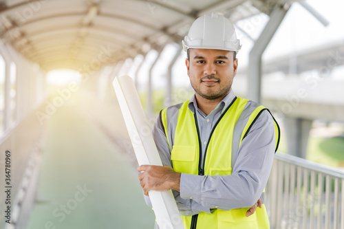 Portrait engineer handsome man or architect looking construction with blueprint and white safety  helme in construction site.