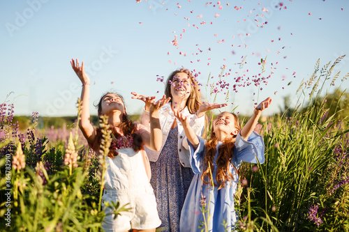 Happy mother and two little daughters play outdoors in the summer park. Family lifestyle. Mom is relaxing with the children on the green grass. 