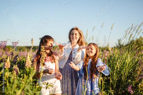 Happy mother and two little daughters play outdoors in the summer park. Family lifestyle. Mom is relaxing with the children on the green grass. 