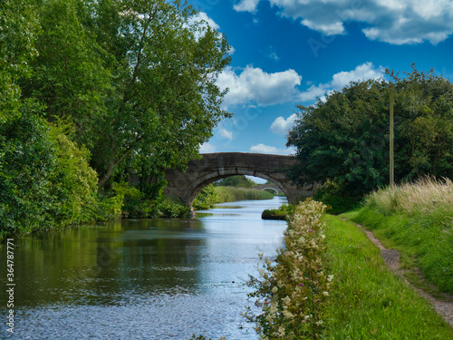 Two bridges on a quiet  rural section of the Leeds to Liverpool Canal in Lancashire  UK. Taken on a sunny day with blue sky and white clouds in summer.