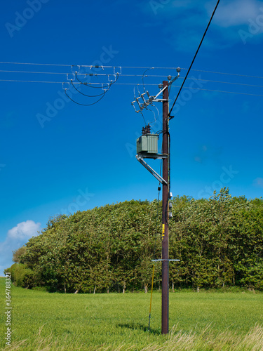An electricity supply pylon delivering power through the UK national grid showing power cables, isolators and other equipment. Taken on a sunny day with a blue sky.