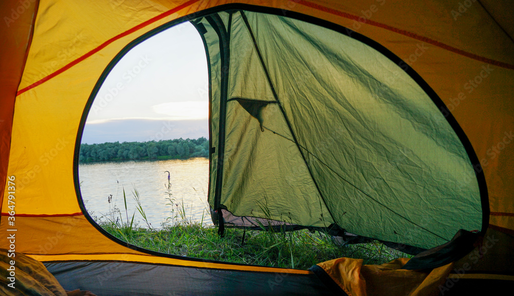 A tent with an open window stands on the banks of the river. From the open tent you can see the river