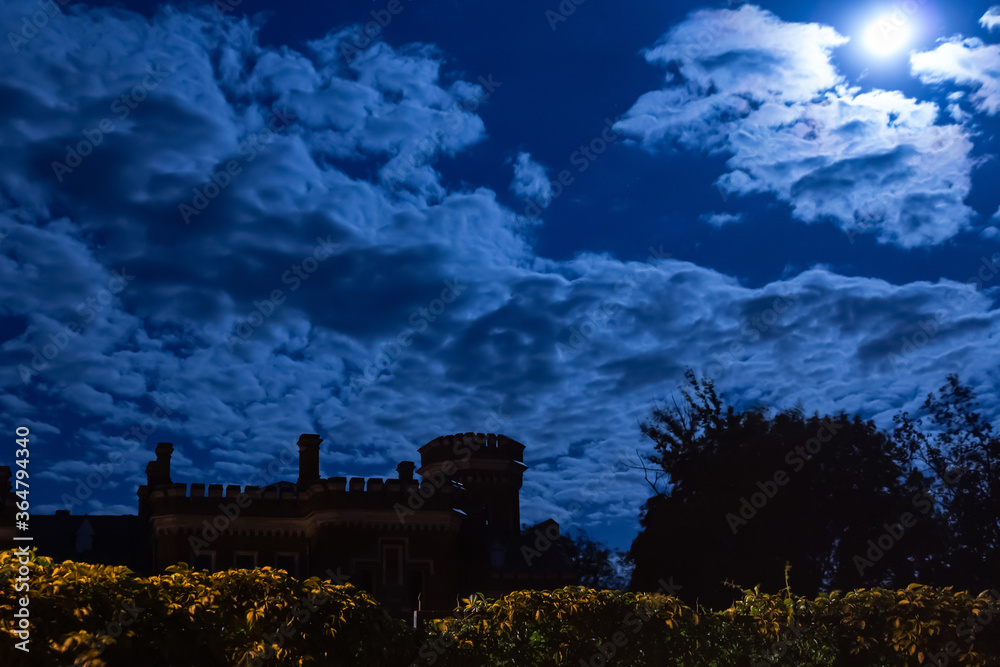 above the castle the night sky with clouds, through the clouds the moon is edging