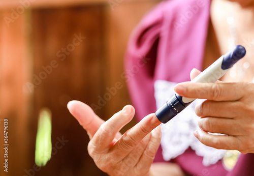 Close up of old woman hands using lancet on finger to check blood sugar level by Glucose meter. Use as Medicine  diabetes  glycemia  health care and people concept.