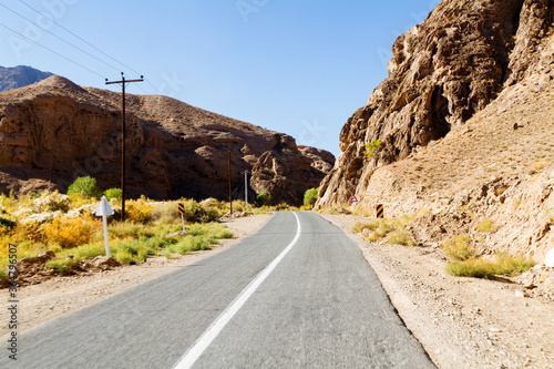 Beautiful scenic view - twisty road across the dry arid land between barren mountains against the background of vivid blue sky. Road to Abyaneh, Iran