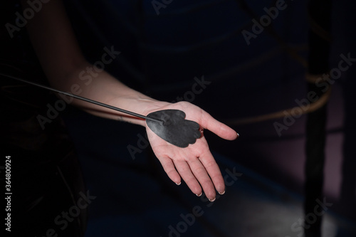 An unrecognizable woman demonstrates an elegant thin leather strip whip in a dark bedroom. Close-up of female hands with a bdsm toy. Pain and pleasure.Adult toy for slaps.