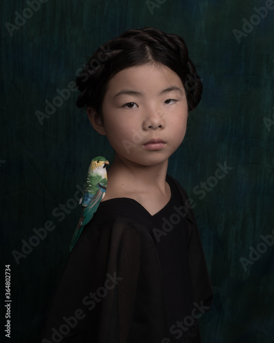 Studio portrait in painterly renaissance style of a little girl wearing black dress with a green bird on her shoulder  photo