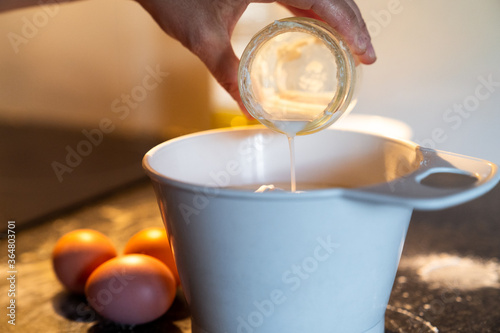 Pour a glass of milk into a recipient to prepare a recipe. Preparation of a homemade cake at home.