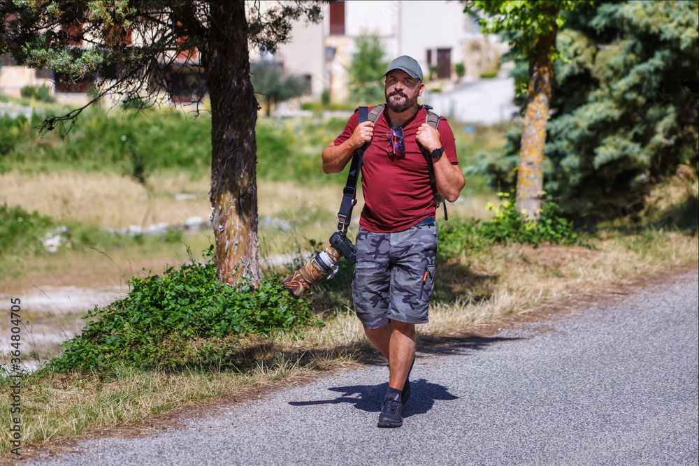 Nature photographer explores a mountain path. Mountain hiker photographer explores the area for the photographic hunting of wild animals. The man carries the backpack on his shoulders with photography Nature photographer explores a mountain path. Mountain hiker photographer explores the area for the photographic hunting of wild animals. The man carries the backpack on his shoulders with photography
