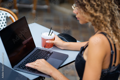 Young woman working with a laptop computer and drinking a cocktail at a bar terrace