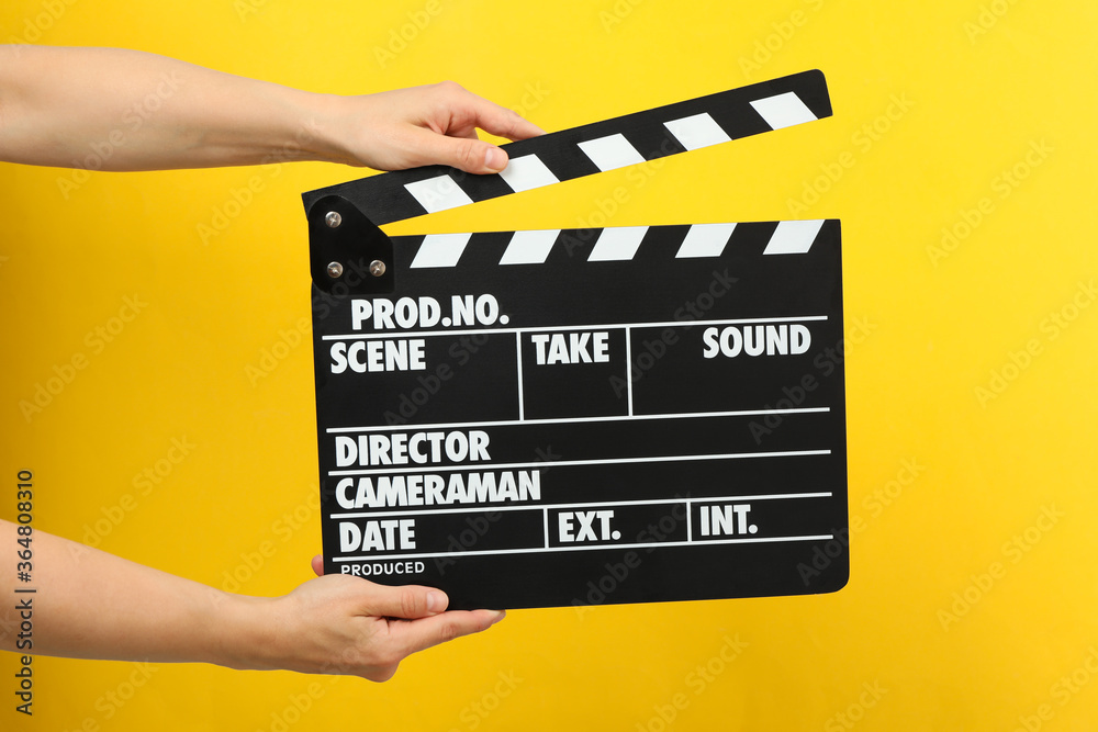 Female hands holding clapper board on yellow background