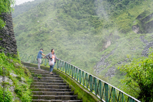 Couple standing on a series of steps with clouds mist and fog on the beautiful green hills of Triund trek in McLeodganj himachal pradesh