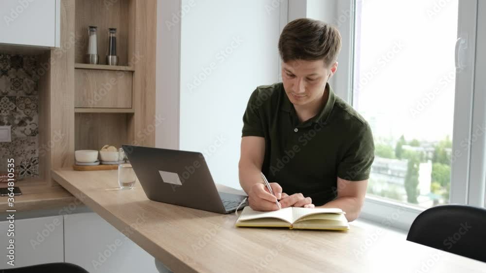 Freelancer work at the laptop and write some notice in a paper notebook. Work from home and stay healthy due the pandemic situation concept Freelancer work at the laptop and write some notice in a paper notebook. Work from home and stay healthy due the pandemic situation concept