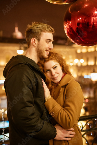 A happy couple stands in an embrace on the street in the evening in the festive lights
