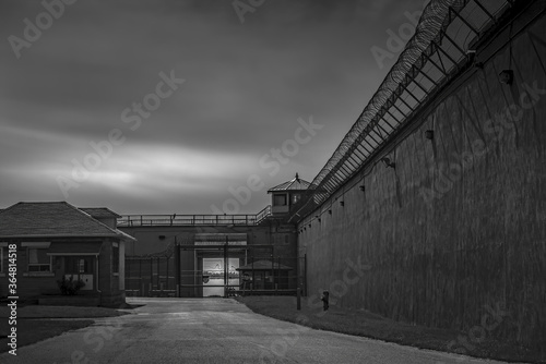 Fototapeta Naklejka Na Ścianę i Meble -  View in yard behind  the exterior walls of Kingston Penitentiary showing high stone walls, barbed wire and guard tower nobody