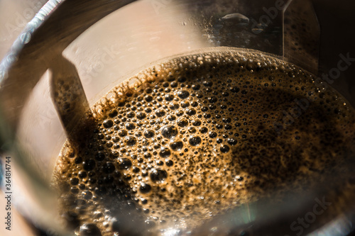 Close up of fresh coffee bubbles in a french press (sometimes called a cafetiere) in sunlight.