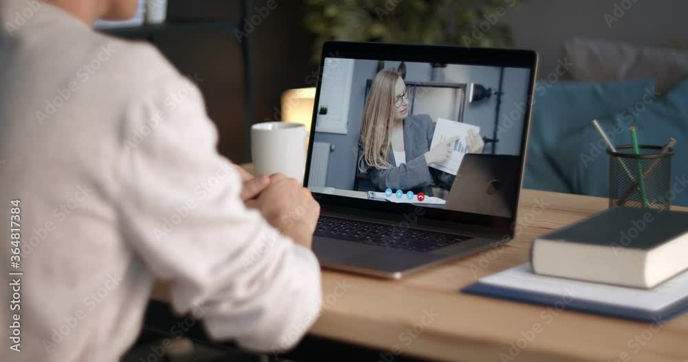 Back view of businesswoman sitting at home and using laptop for video chat. Mature lady having online conversation with female colleague that showing financial report with graphs on video.