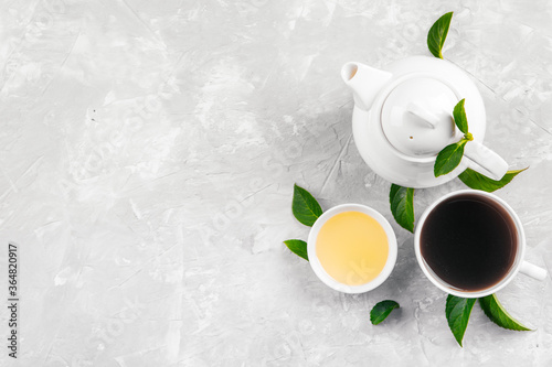 Herbal tea, cups and teapot with leaves on grey concrete background. Flat lay.