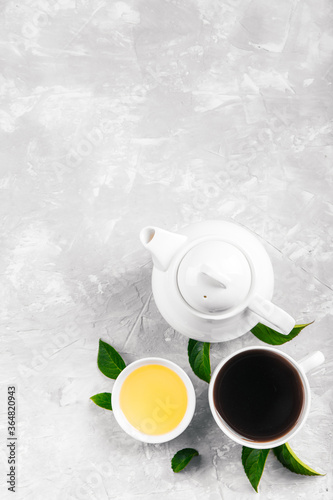 Herbal tea, cups and teapot with leaves on grey concrete background. Flat lay.