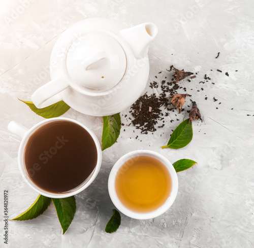 Herbal tea, cups and teapot with leaves on grey concrete background. Flat lay.