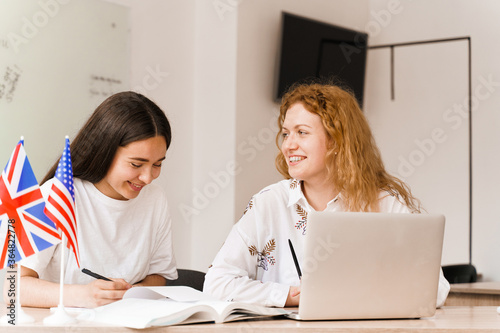 Foreign school private study with a school girl. Teacher explain grammar of native language using laptop. Prepearing to exam with tutor. English and British flags in front.