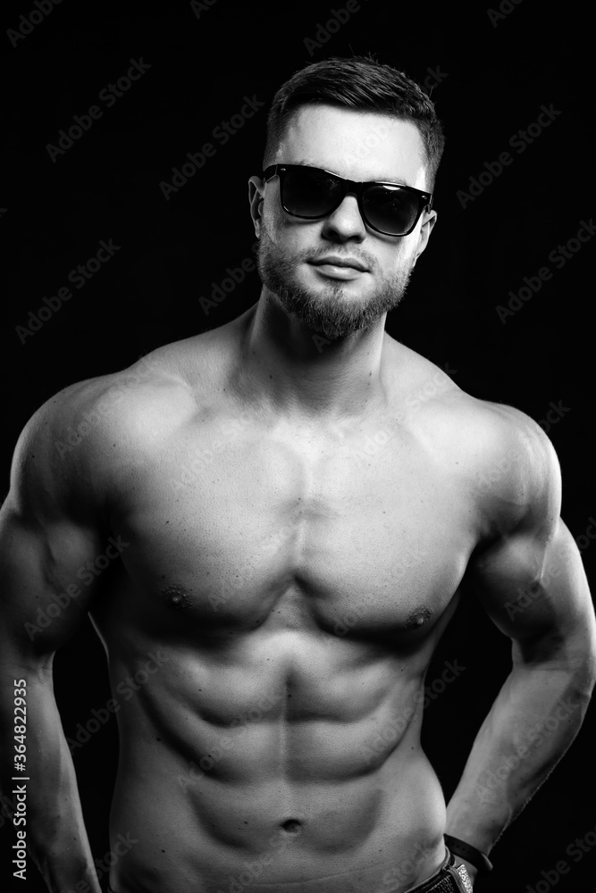 Fototapeta premium Muscular guy with naked torso posing with hands on waist. Studio photo. Portrait of a handsome man in jeans. Black and white.