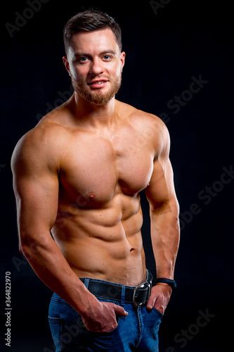 Strong athletic man fitness model torso showing six pack abs. Isolated on dark background. Half length photo.