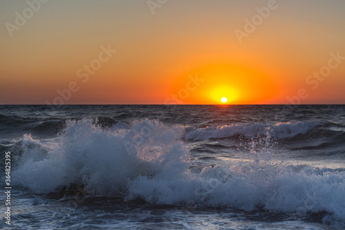 Sunset and storm at sea. Large waves against the background of the setting sun. Summer storm on the Black sea. Beautiful sea spray on the rocks.