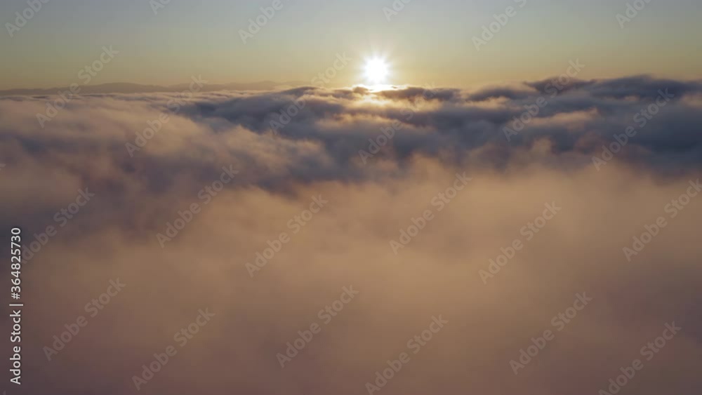 Flying through heavenly amazing sunny cloudscape toward the sun rising over the horizon and shining through the golden fluffy fog. Beautiful timelapse of clouds moving softly on the sky. 4K B roll