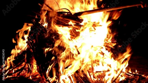 Camp fire in the night, or evening fire. A man with a garden fork turns the firewoods from the fire