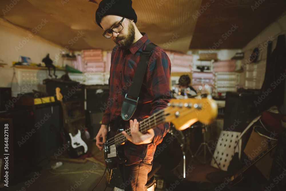 Young man playing bass guitar during rehearsal in garage Young man playing bass guitar during rehearsal in garage