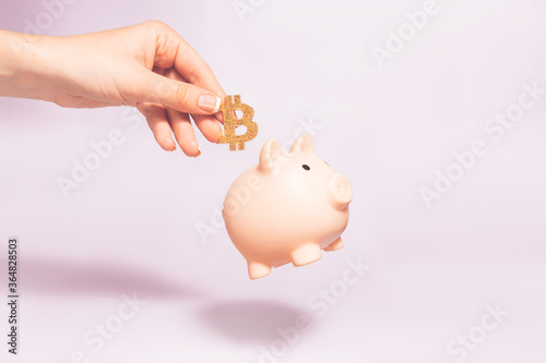 Bitcoin holding concept. Piggy bank for bitcoins. Cryptocurrency saving symbol. A woman puts bitcoin in a money box on a pastel background. Copy space.