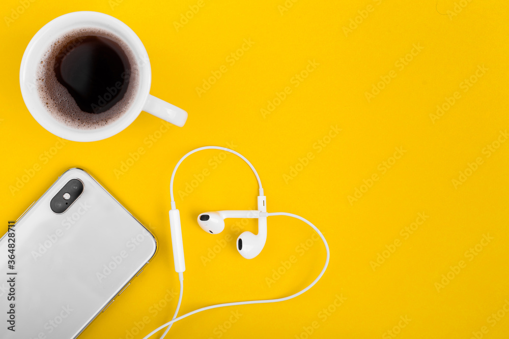 View from above at the phone, coffee and headphones in the form of heart on the yellow desk. View from above at the phone, coffee and headphones in the form of heart on the yellow desk.