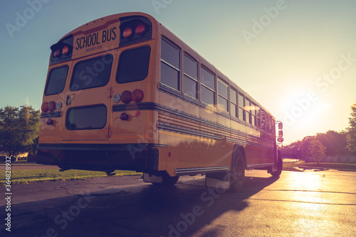 Back right low angle view of American Public school bus driving away with sunset in the distance