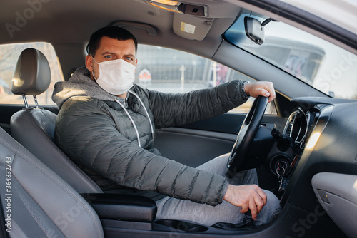 A young man sits behind the wheel wearing a mask for personal safety while driving during a pandemic and coronavirus. Epidemic © Andrii