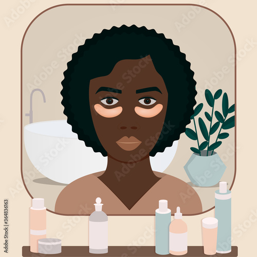 Young African woman looks at the mirror in bathroom. Applying eye patches under eyes to moisturize face skin. Skin care and treatment spa procedure at home. Girl’s head at mirror view.