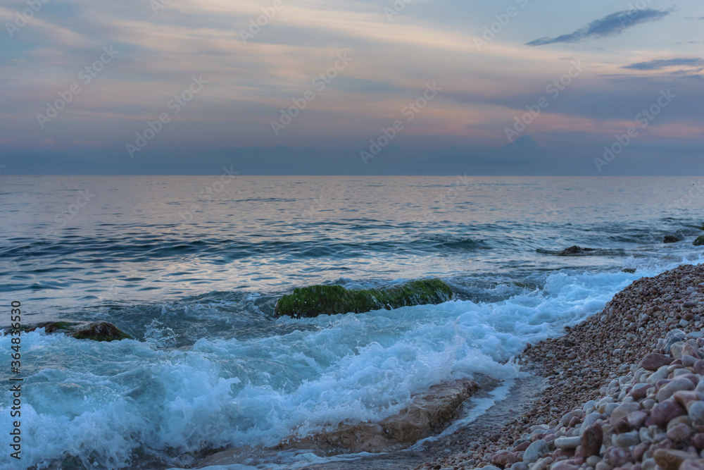 Seashore in the evening. Beautiful blue light. Landscape with pebbles in small waves. The coast of the sea without people. Relaxing sea background.