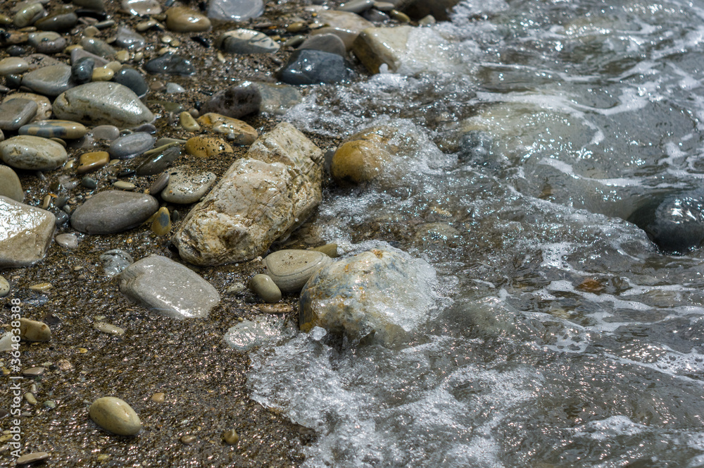 pebble stones on the sea beach, the rolling waves of the sea with foam