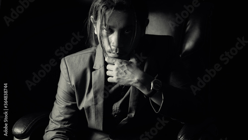 A long haired young business man wearing a suit thinking on revolving chair in darkness.