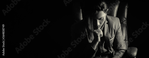 A long haired young business man wearing a suit thinking on revolving chair in darkness.