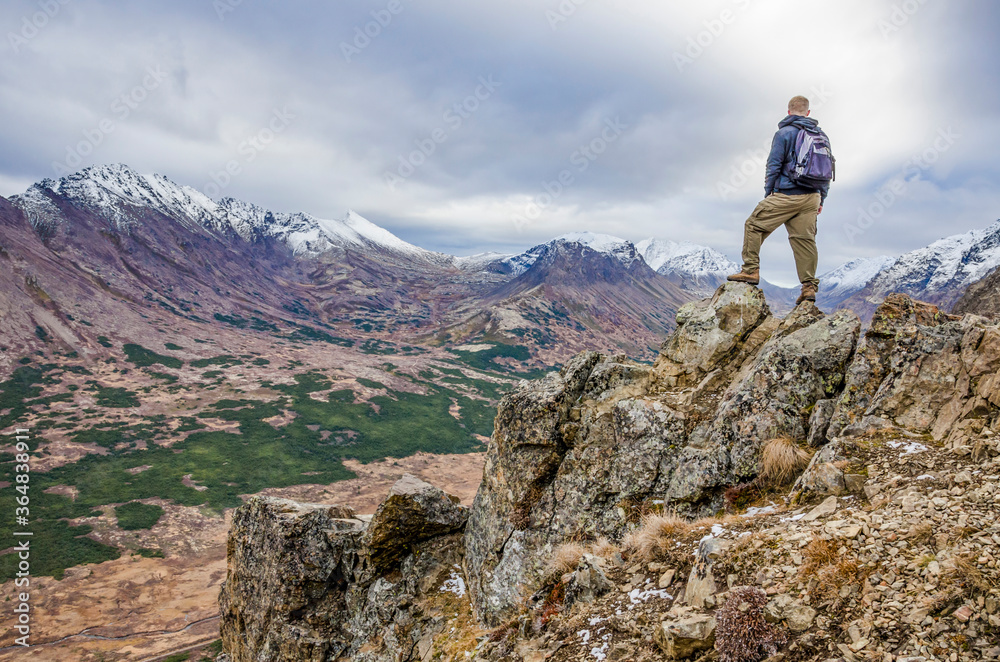 Adventurous man standing on the side of a mountain looking at the open landscape on a cloudy day.