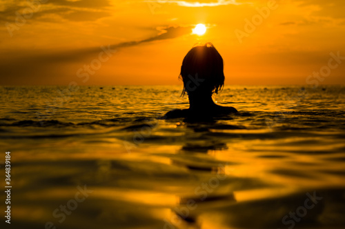 Girl swimming in the sea at sunset  splashes of transparency water  female black silhouette