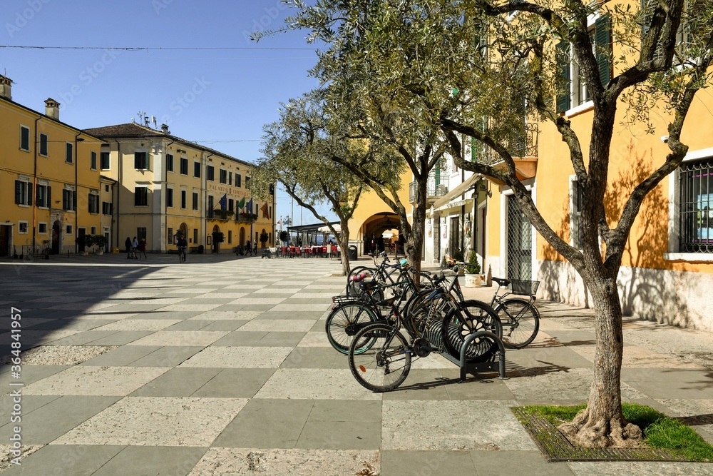 View of the main square of the old town on the shore of Lake Garda with bicycles parked under a row of olive trees, Lazise, Verona, Veneto, Italy