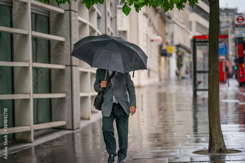 Middle-aged businessman wearing a suit caught out in the rain during a windy  drizzly day fighting the wind under an umbrella in Holborn  London during the COVID-19 pandemic 101