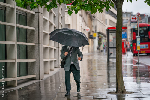 Принти на полотні Middle-aged businessman wearing a suit caught out in the rain during a windy  dr