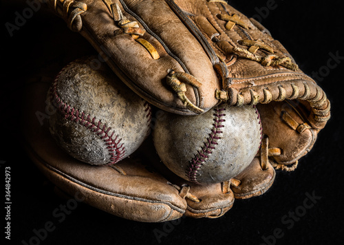 Two worn baseballs in an old mitt on black background. © DCrane Photography
