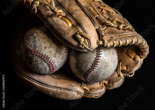 Fotografie Two worn baseballs in an old mitt on black background.