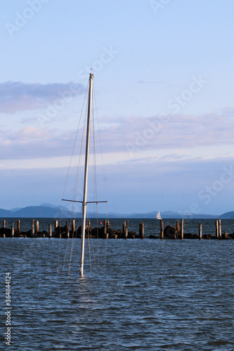 фотографія The solitary and fully rigged mast of a sunken sail boat stands in the calm water of a deserted inner harbor