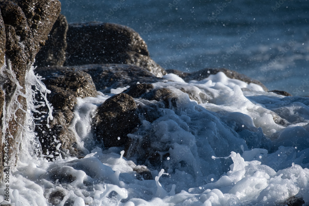 Close up of foamy white waves splashing over rocks on the ocean shore Close up of foamy white waves splashing over rocks on the ocean shore