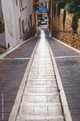 Narrow alley with two tracks for car wheels and stairs in the middle, Polop de Marina, Spain © Loes Kieboom
